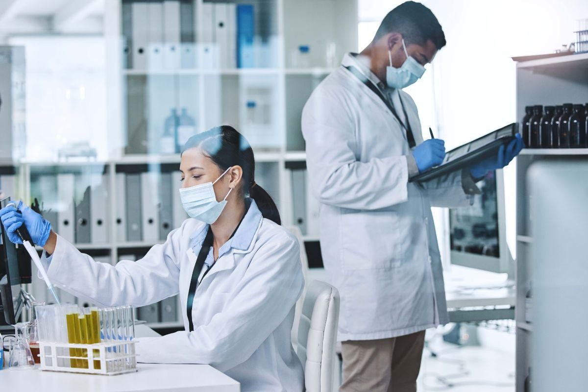 Two researchers working in a lab, one using a pipette and the other taking notes.
